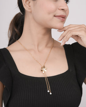 Close-up of woman wearing gold flower pendant necklace with pearl accents on gold chain, black ribbed top