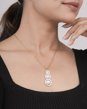 Close-up of woman wearing gold chain necklace with triple pearl pendant and black top