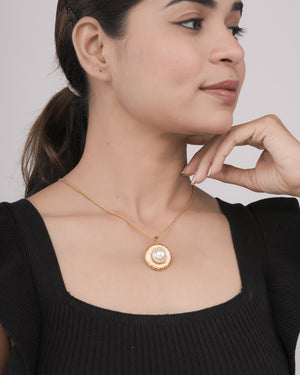 Close-up of woman wearing a gold necklace with a large pearl pendant, dressed in black top