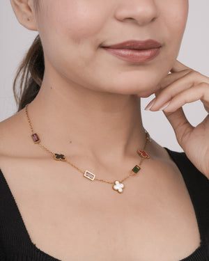 Close-up of a woman wearing a gold chain necklace with colorful rectangular and clover-shaped gemstone charms