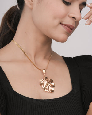 Close-up of woman wearing elegant gold flower pendant necklace with black top against light background