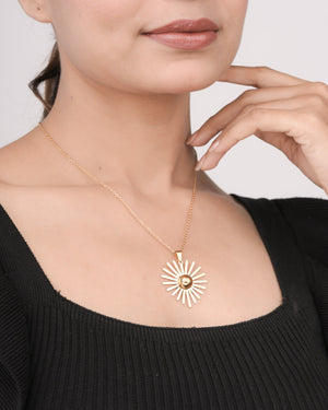 Close-up of woman wearing a gold sunburst pendant necklace and black ribbed top