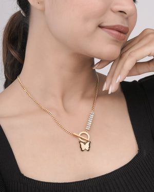 Close-up of woman wearing a gold chain necklace with butterfly pendant and crystal accents, styled with black top