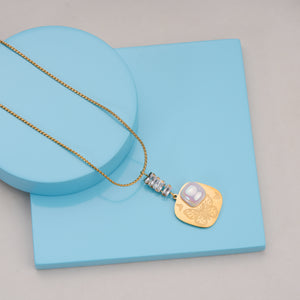 Gold chain necklace with pendant featuring butterfly engraving, pearl detail, and crystal accents on blue display