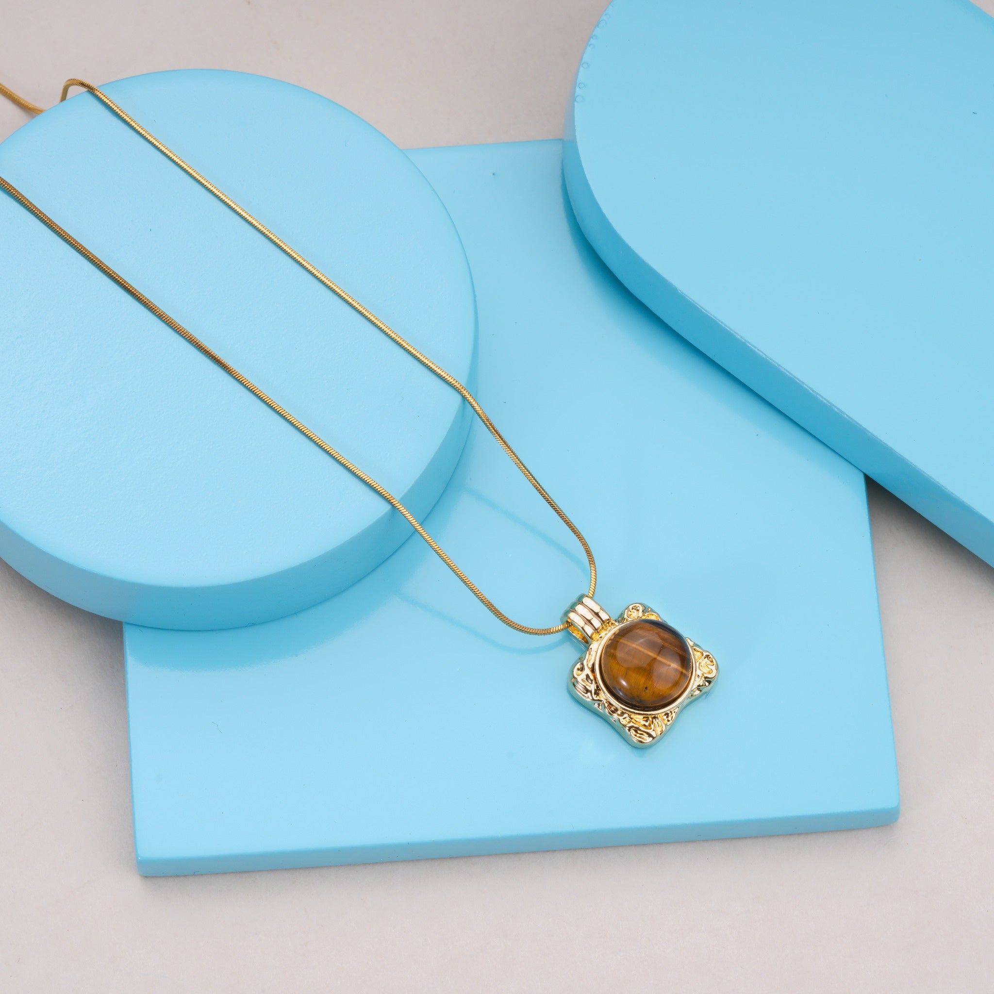 Gold necklace with tiger eye gemstone pendant on light blue display blocks
