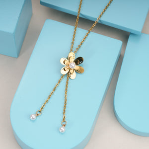 Gold flower pendant necklace with pearl center and pearl accents on delicate chains, displayed on blue blocks