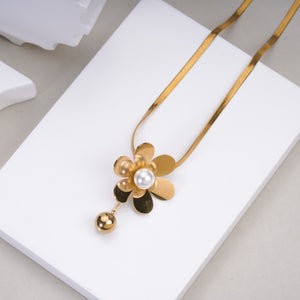 Gold flower pendant necklace with pearl center and dangling bead on white display