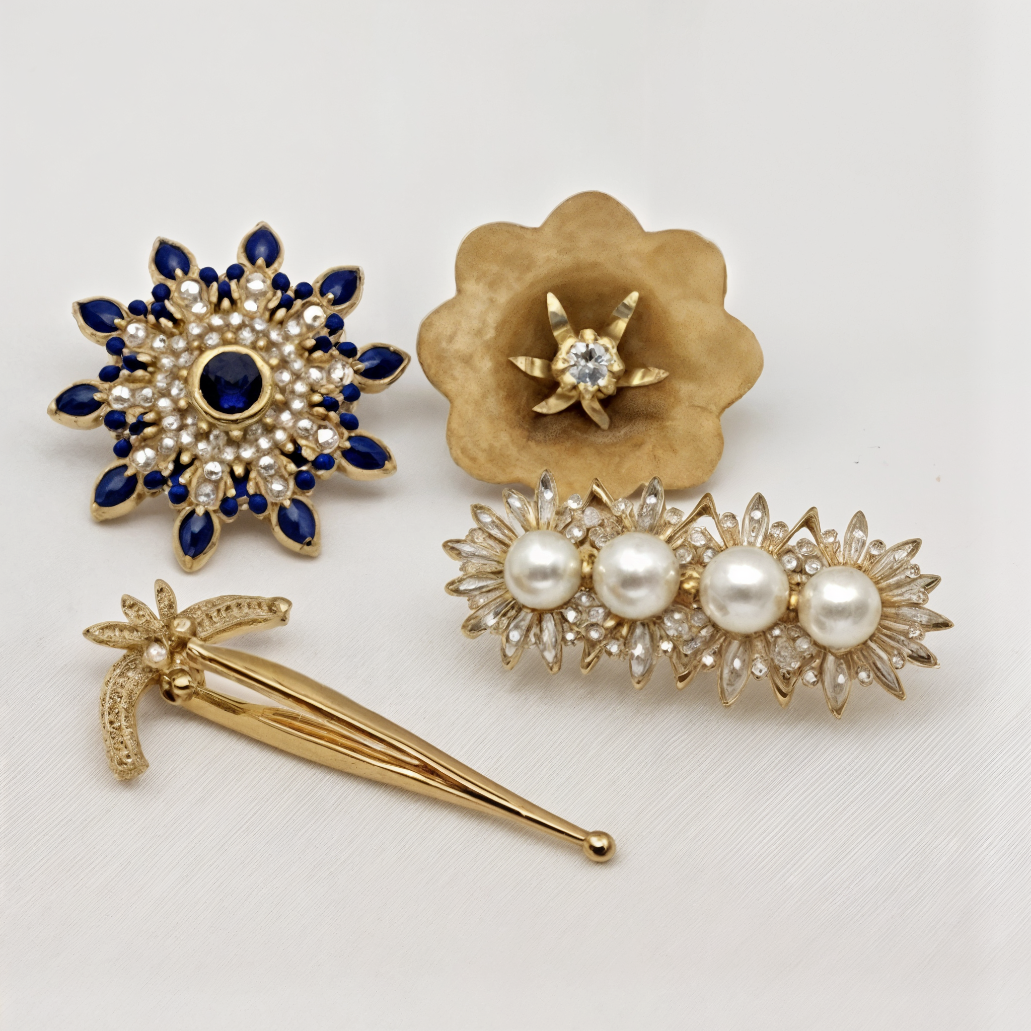Set of four vintage-style gold fashion brooches with blue stones, pearls, and clear crystals on white background
