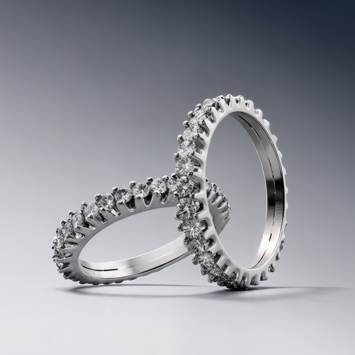 Two stainless steel rings adorned with sparkling round-cut diamonds on gray background