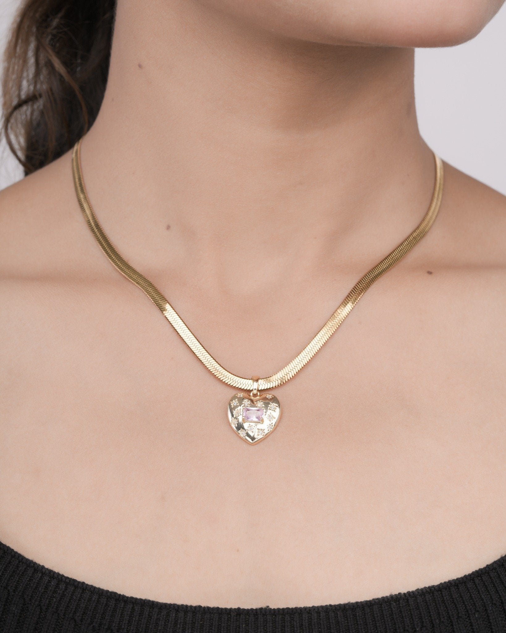 Close-up of a woman wearing a gold heart-shaped pendant necklace with a pink gemstone on a thick gold chain
