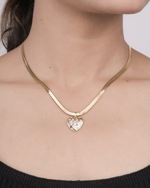 Close-up of a woman wearing a gold heart-shaped pendant necklace with a pink gemstone on a thick gold chain