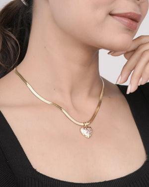 Close-up of woman wearing gold chain necklace with heart-shaped pendant featuring a pink stone, styled with black top