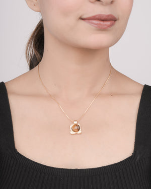 Woman wearing a delicate gold necklace with a square pendant featuring a brown gemstone, styled with a black top