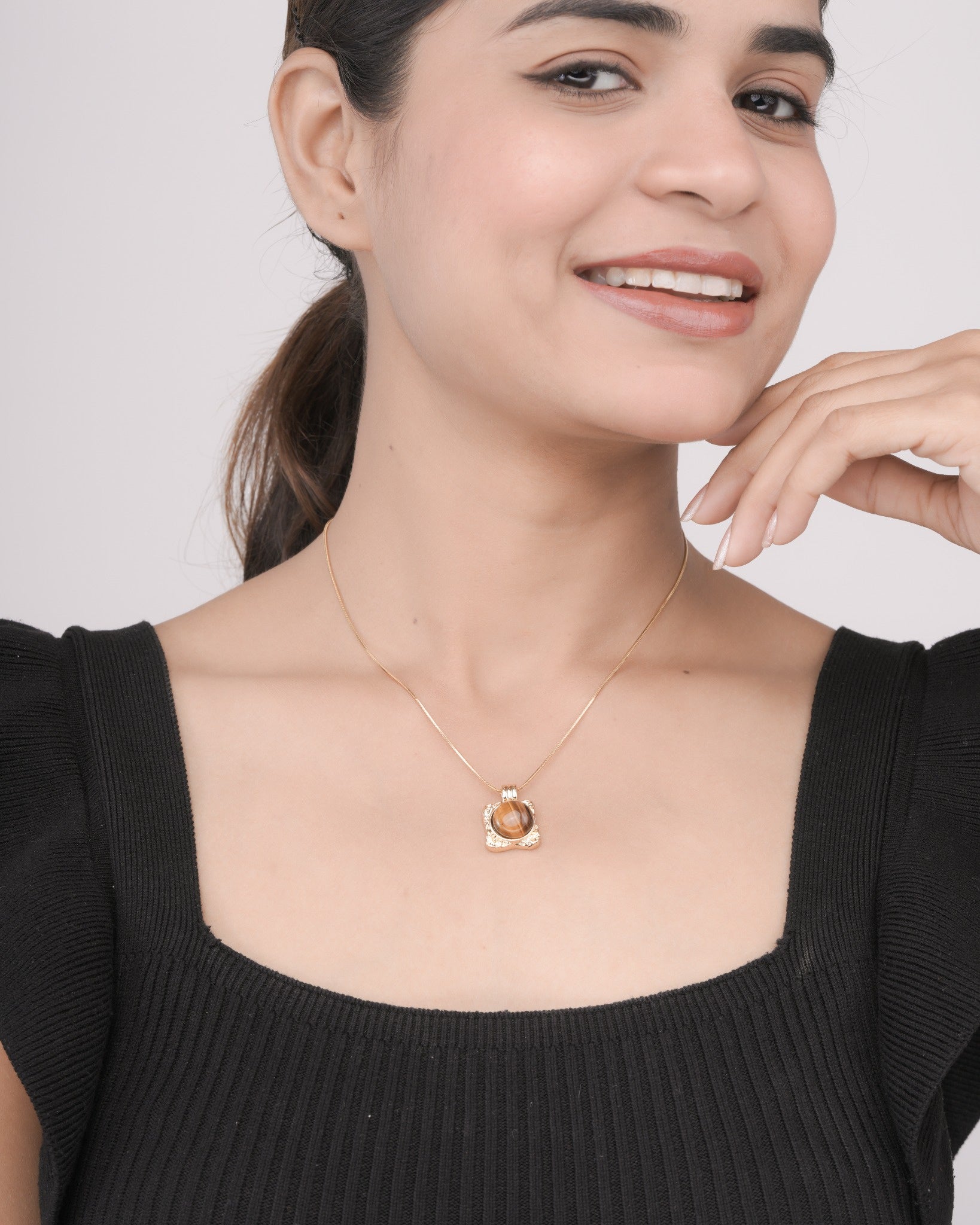 Close-up of woman wearing gold chain necklace with brown stone pendant, black ribbed top, smiling