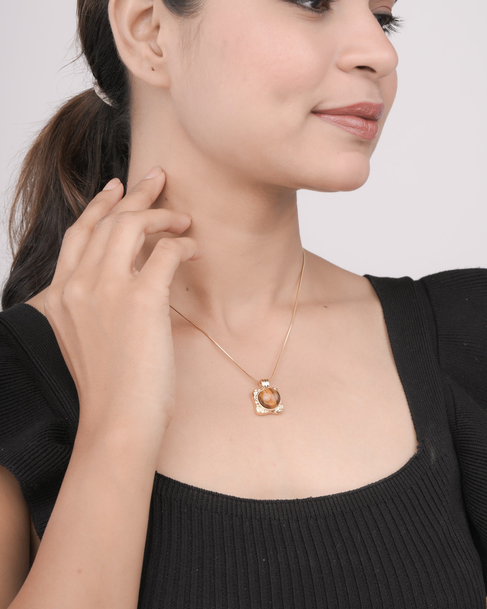 Woman wearing gold pendant necklace with brown gemstone, styled with black ribbed top