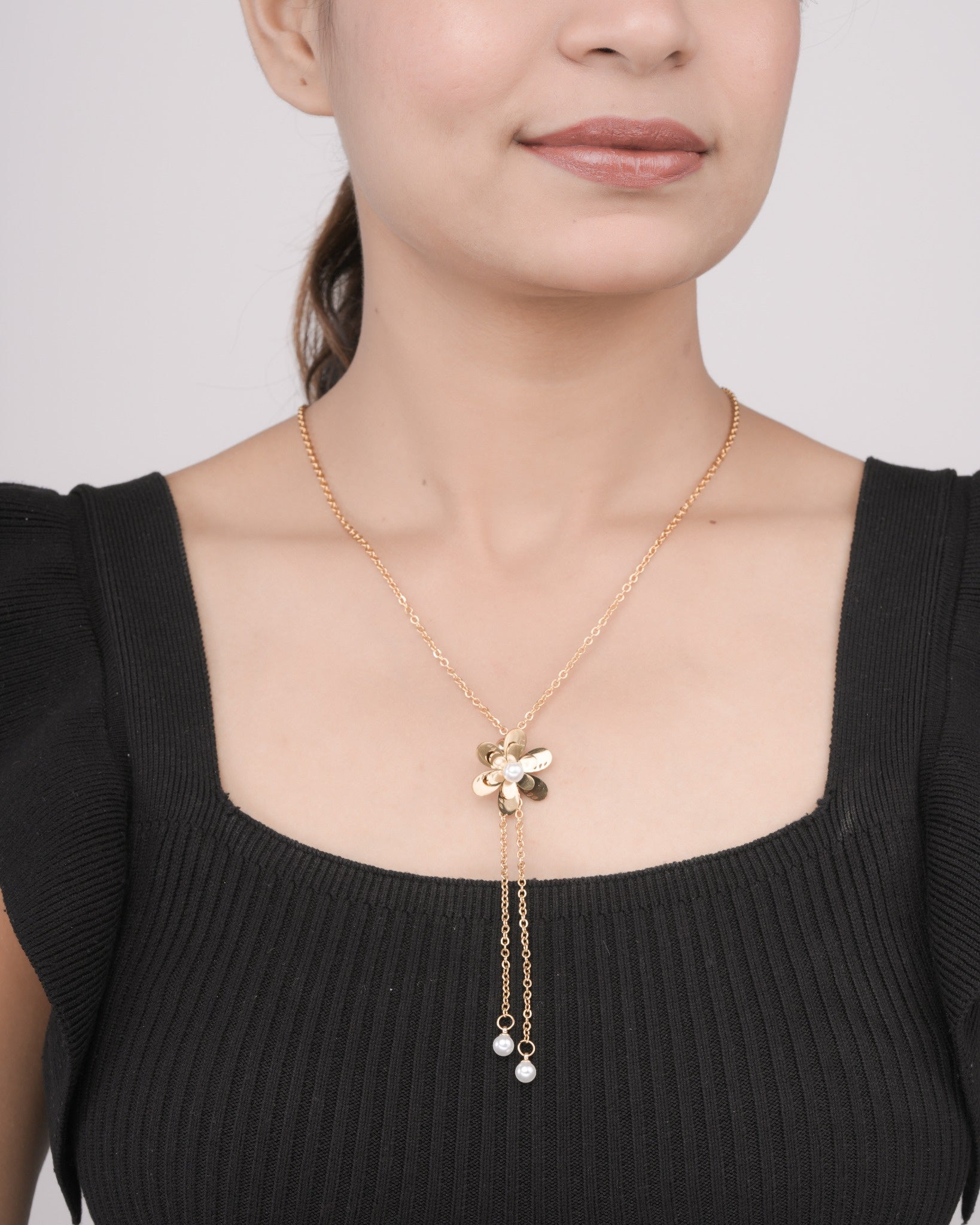 Woman wearing gold floral pendant necklace with pearl accents on gold chain, styled with black ribbed top