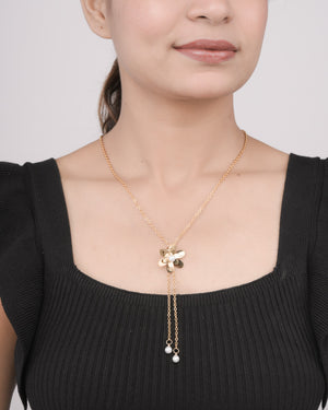 Woman wearing gold floral pendant necklace with pearl accents on gold chain, styled with black ribbed top