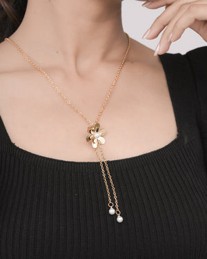 Gold flower pendant necklace with pearl accents on woman wearing black ribbed top