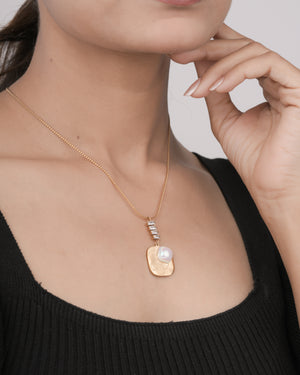Close-up of woman wearing a gold pendant necklace with butterfly engraving and pearl detail, black top