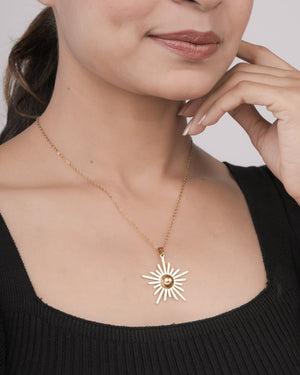 Woman wearing a gold sunburst pendant necklace with a chain on a black top, close-up