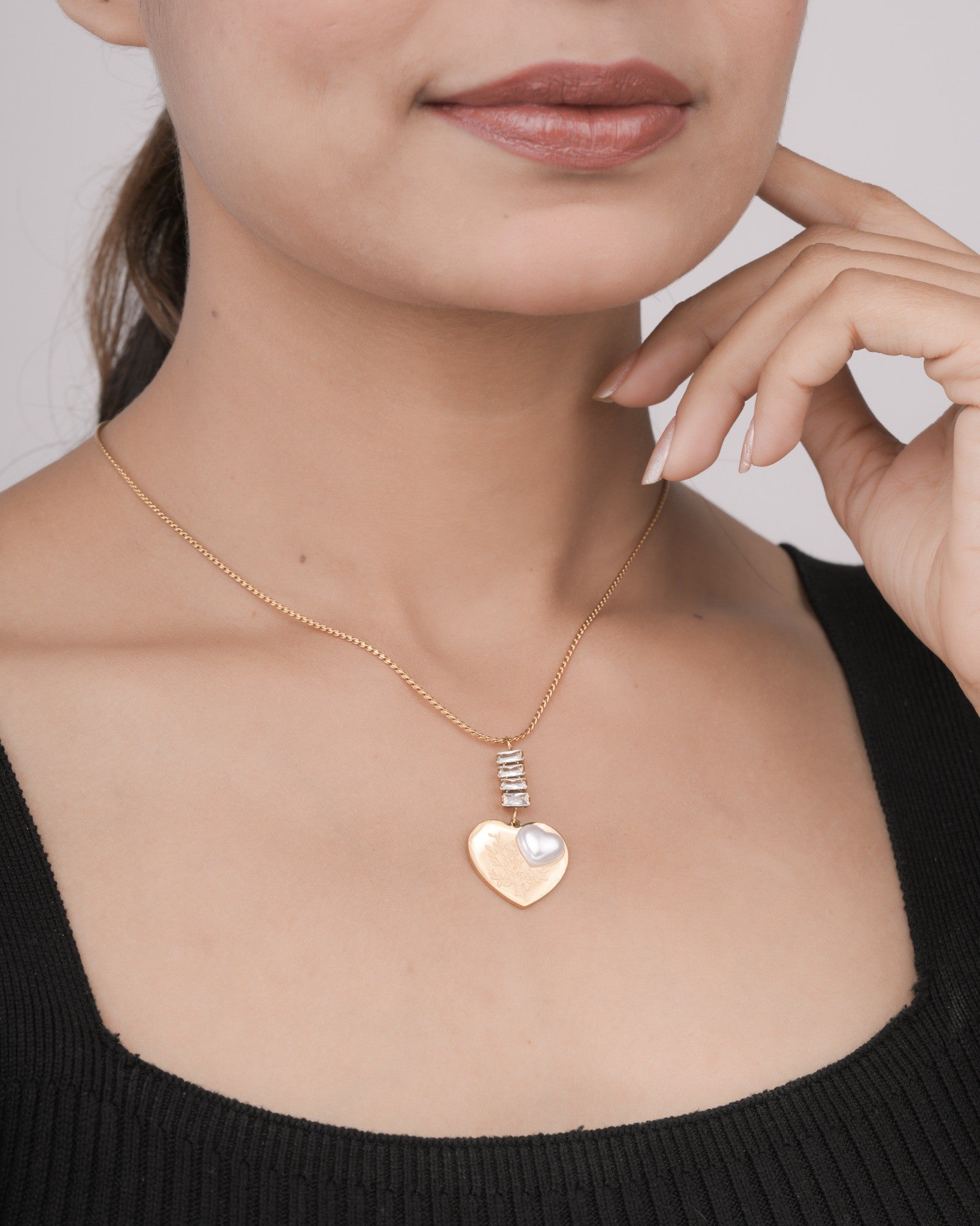 Close-up of woman wearing a gold heart pendant necklace with pearl detail and crystal accents on gold chain