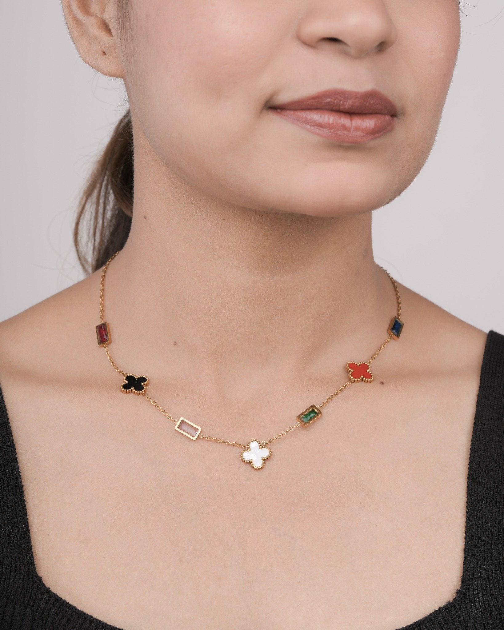 Close-up of a woman wearing a gold chain necklace with colorful rectangular and clover-shaped pendants