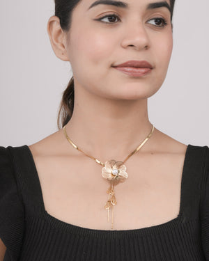 Close-up of woman wearing gold flower pendant necklace with pearl detail, black top background