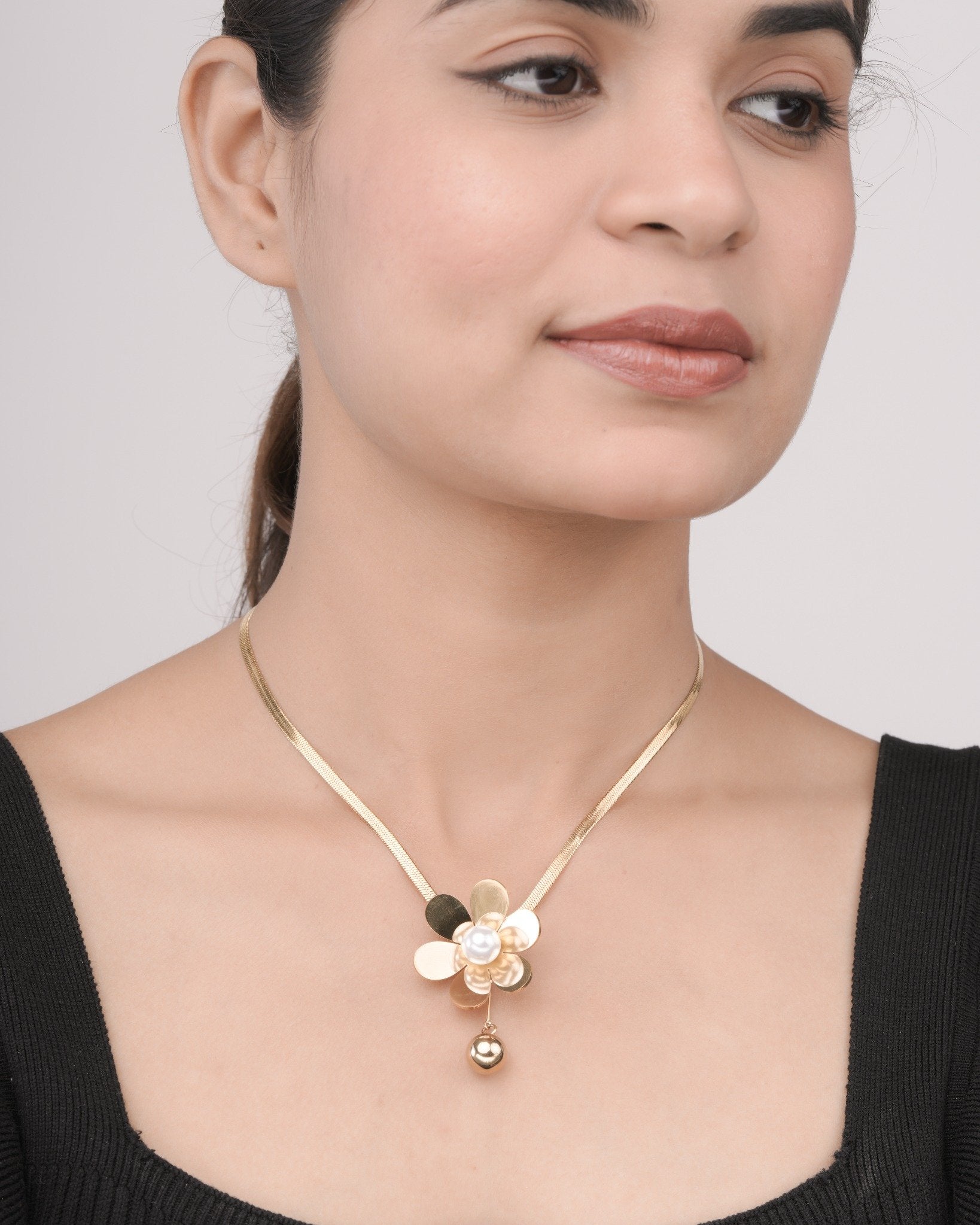 Woman wearing a gold flower-shaped necklace with a pearl center and hanging gold bead, black top