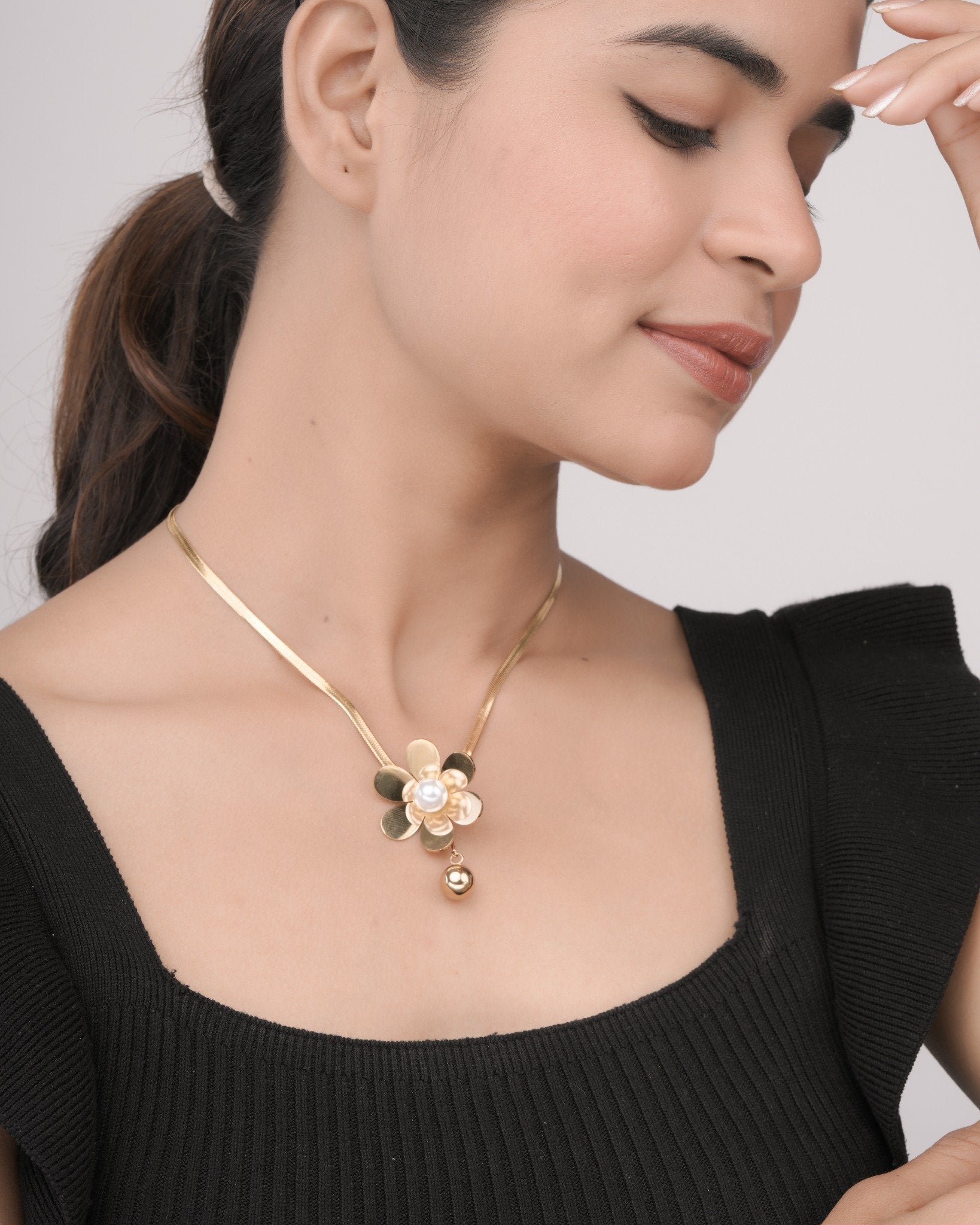 Woman wearing a gold flower pendant necklace with pearl detail on a sleek gold chain, paired with a black top
