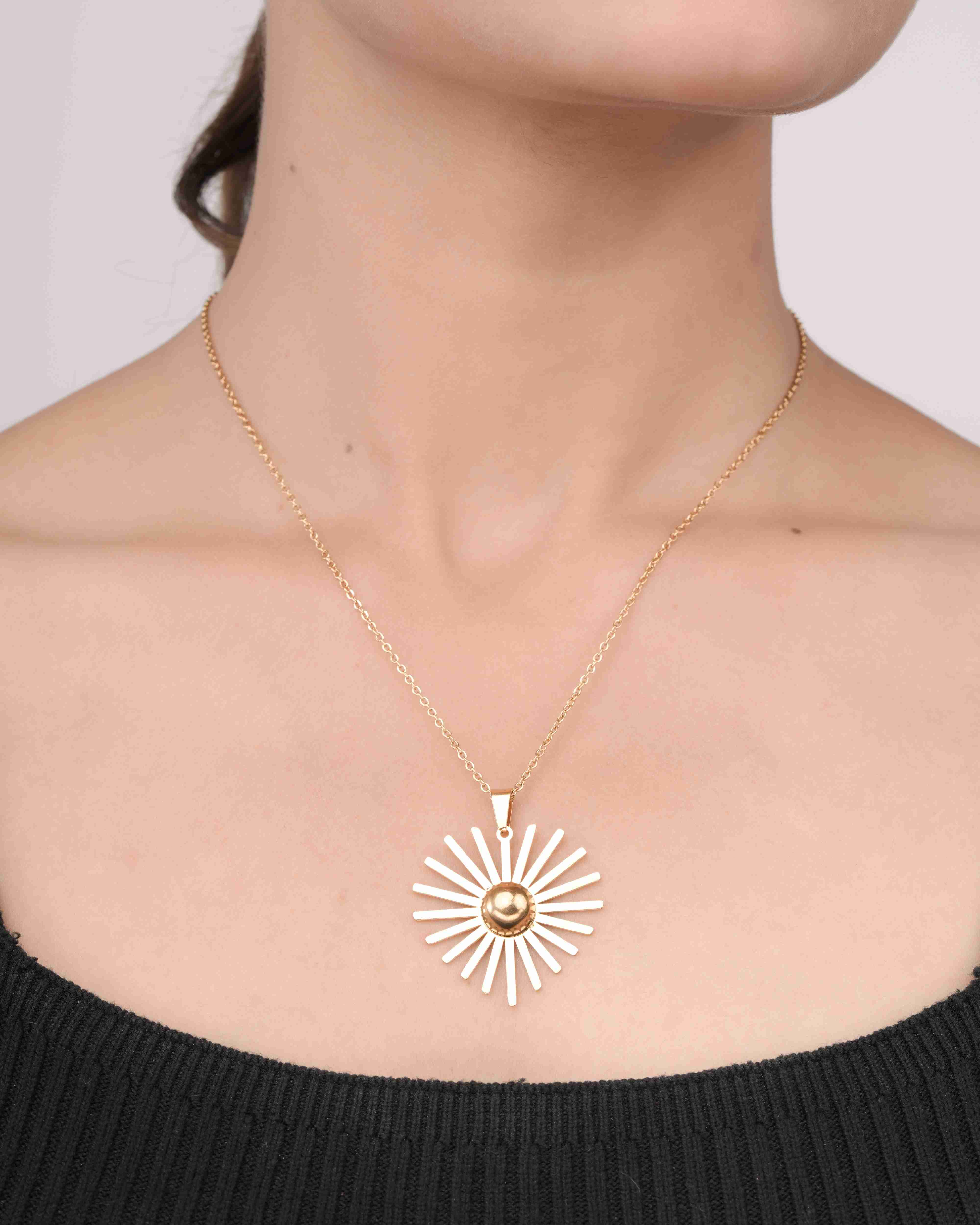 Woman wearing a gold sunburst pendant necklace with white enamel rays on a fine chain