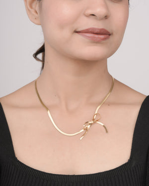 Woman wearing a shiny gold ribbon-shaped necklace with a black square-neck top