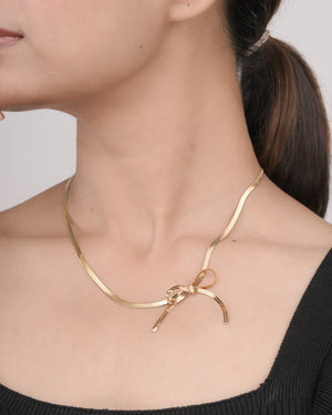 Close-up of woman wearing gold fashion jewellery necklace with bow detail, styled with black top