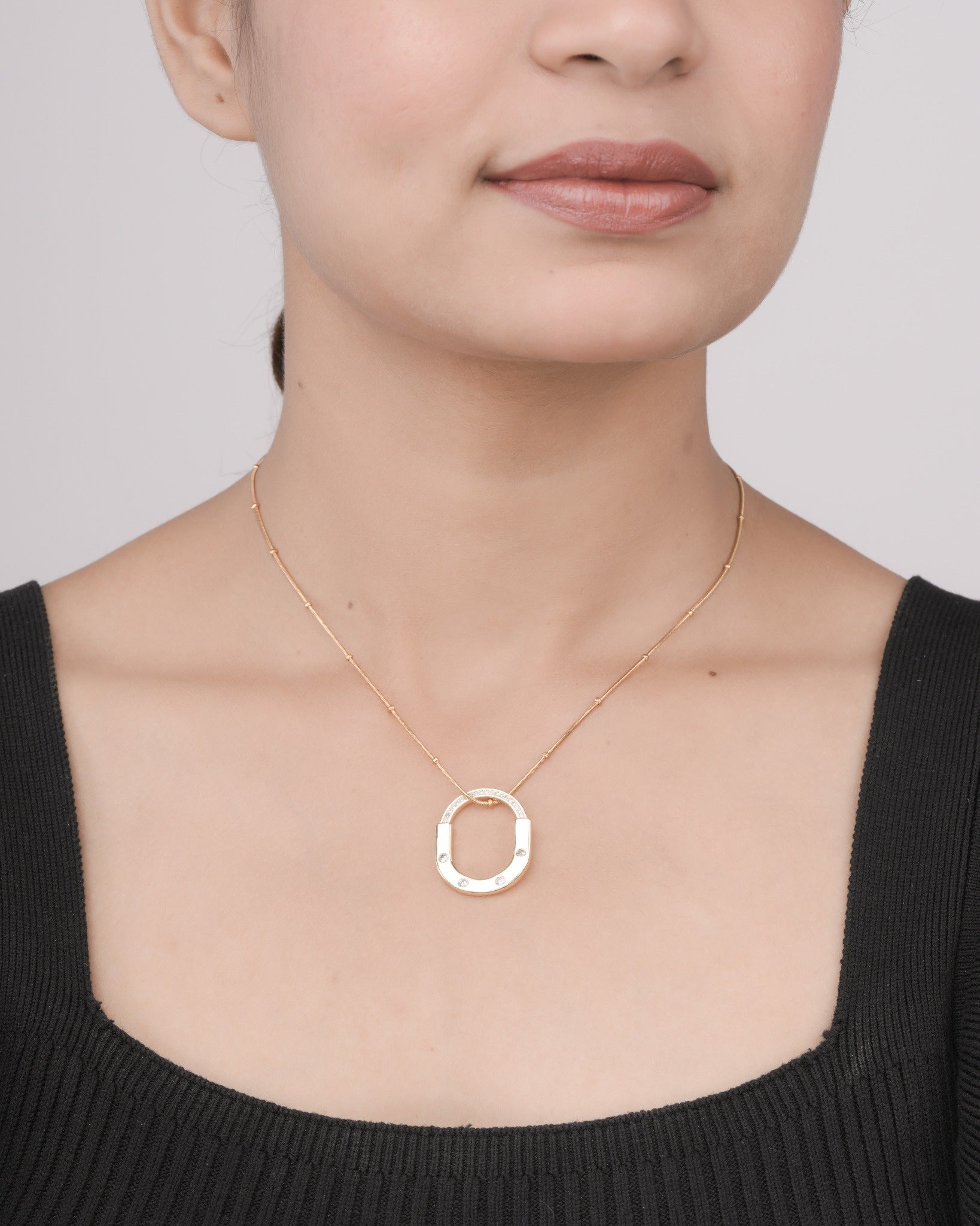 Woman wearing a delicate gold necklace with an oval pendant featuring small embedded crystals, styled with a black top