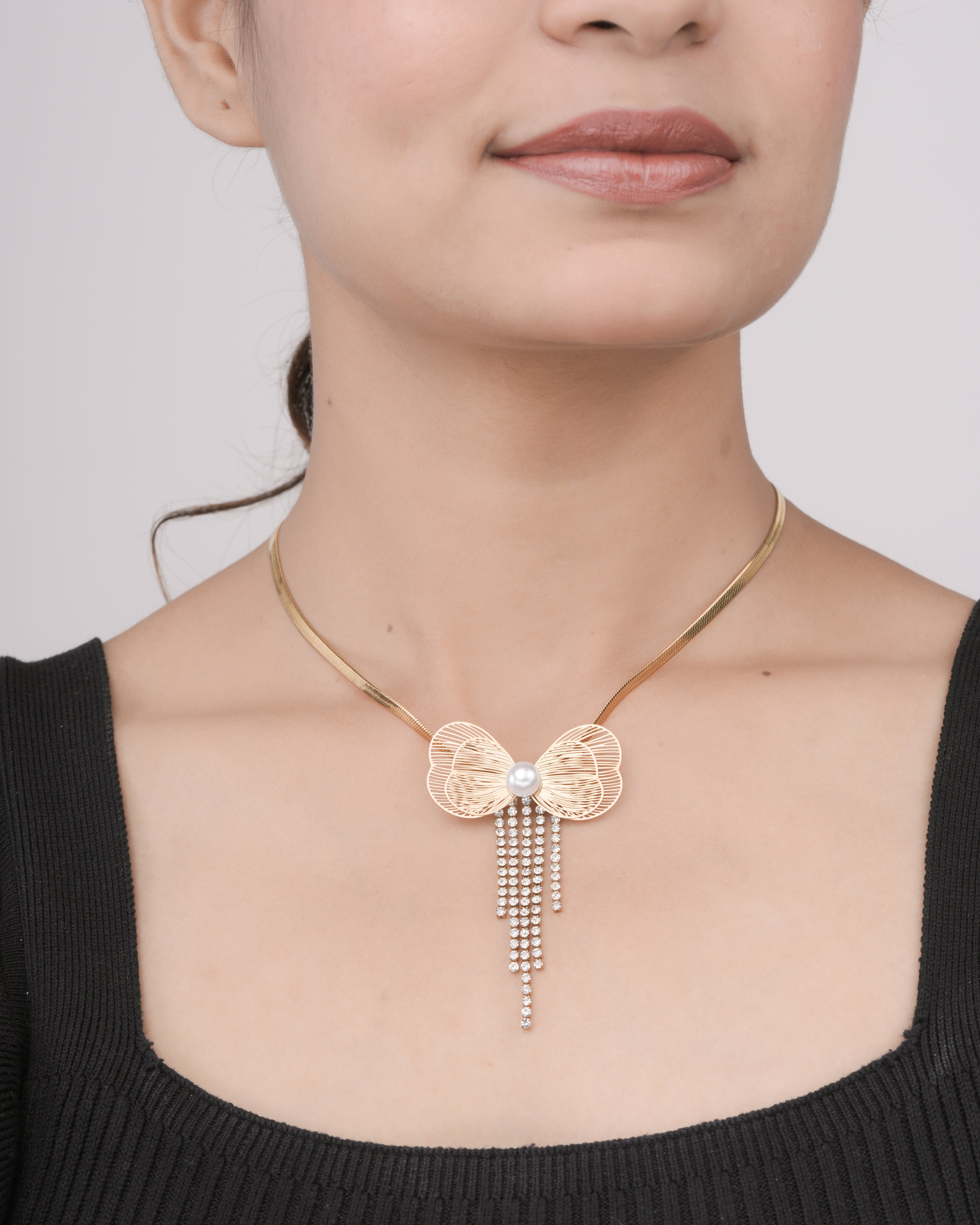 Close-up of woman wearing a gold butterfly pendant necklace with pearl center and dangling crystals