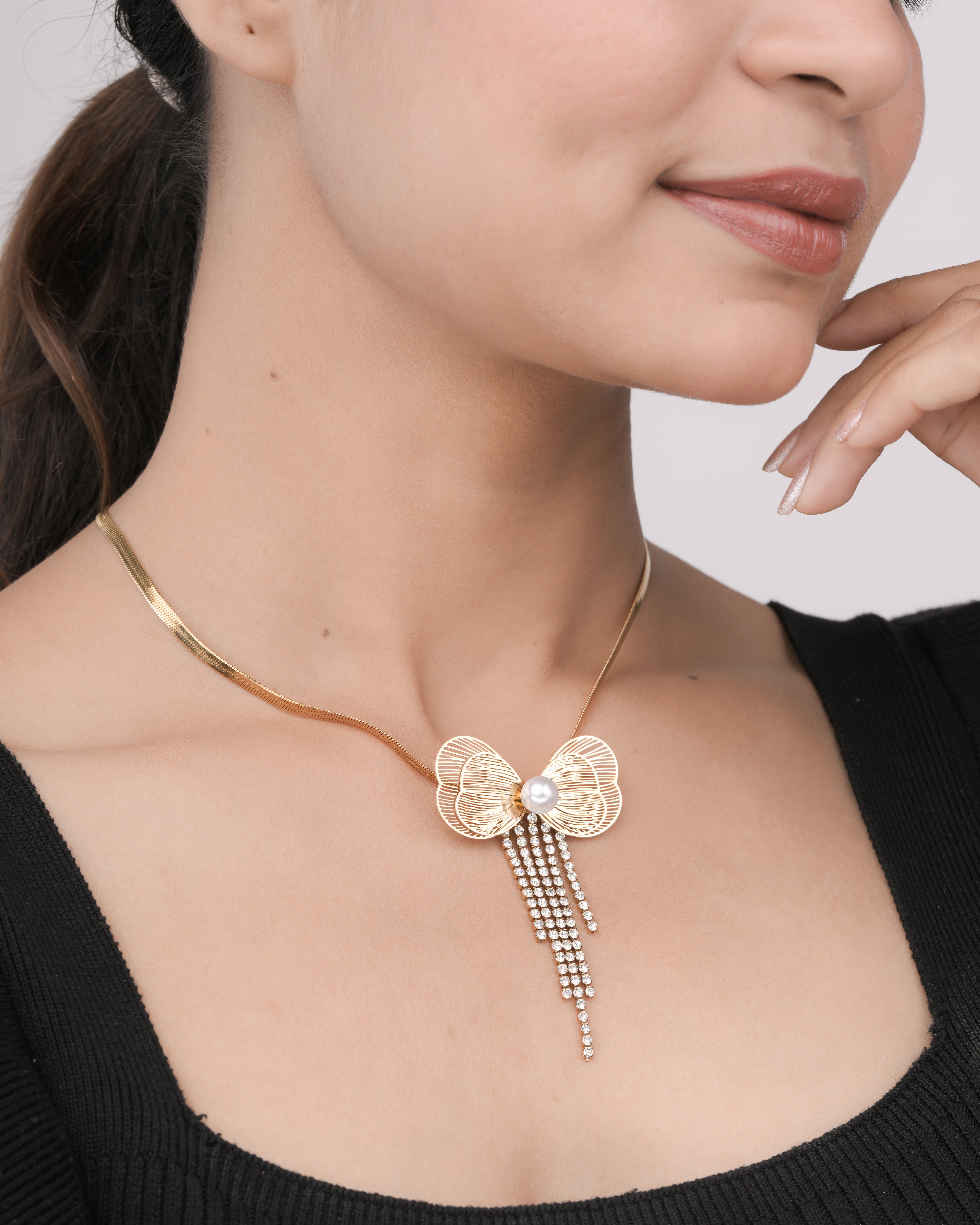 Woman wearing a gold fashion necklace with a bow-shaped pendant featuring a pearl and dangling crystals