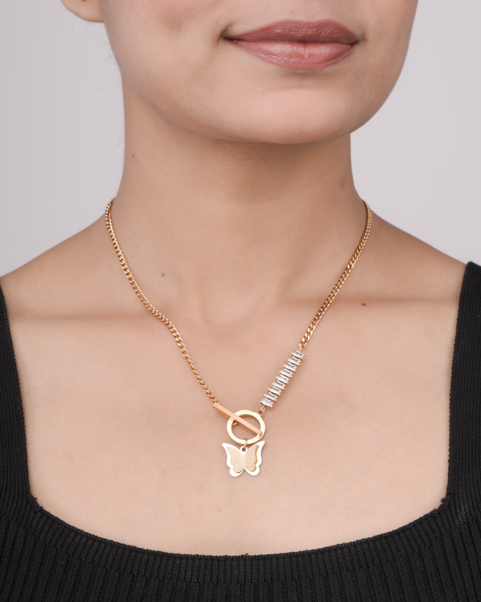 Close-up of a gold chain necklace with a butterfly pendant and crystal accent on a woman's neck wearing a black top
