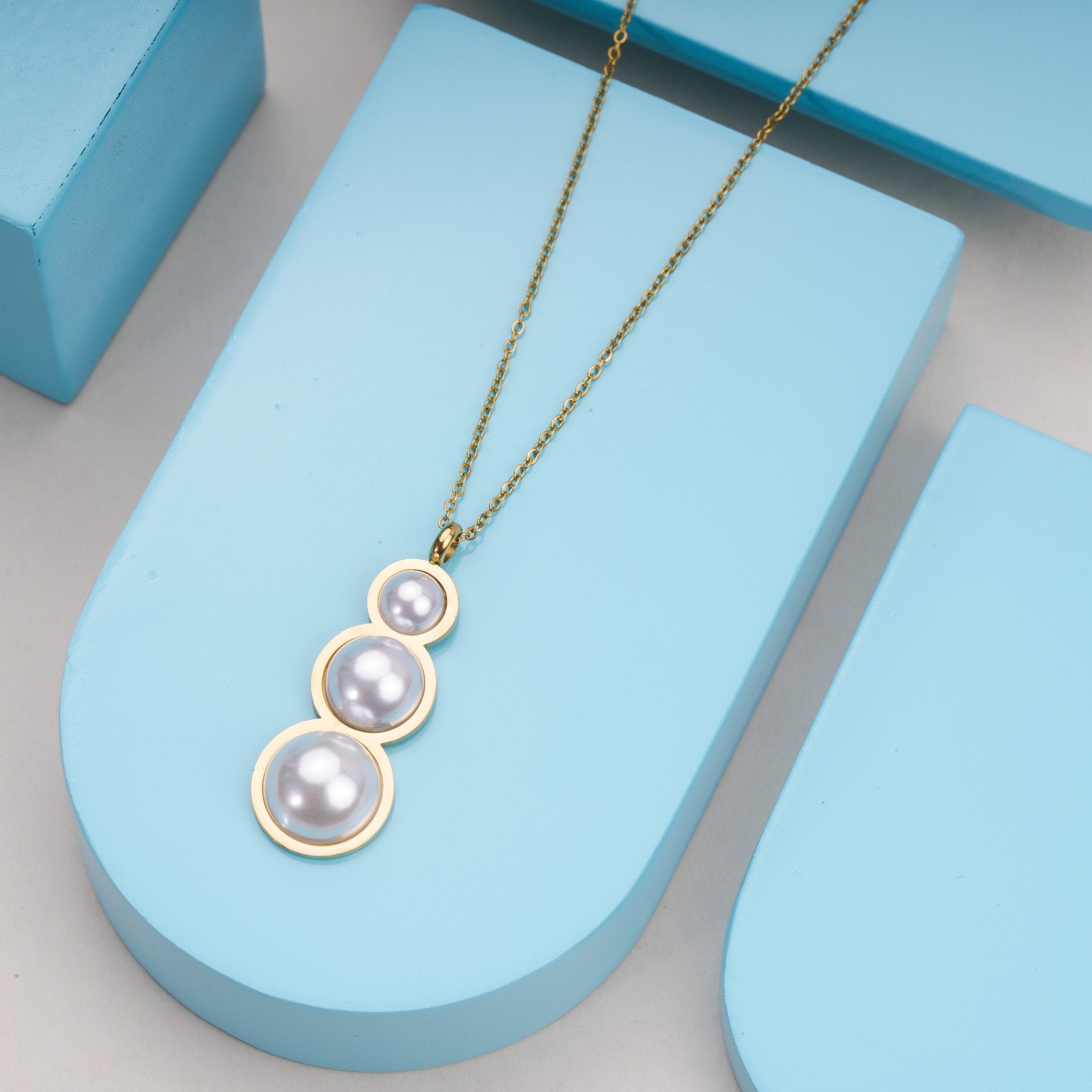 Gold chain necklace with three large pearls pendant displayed on blue blocks