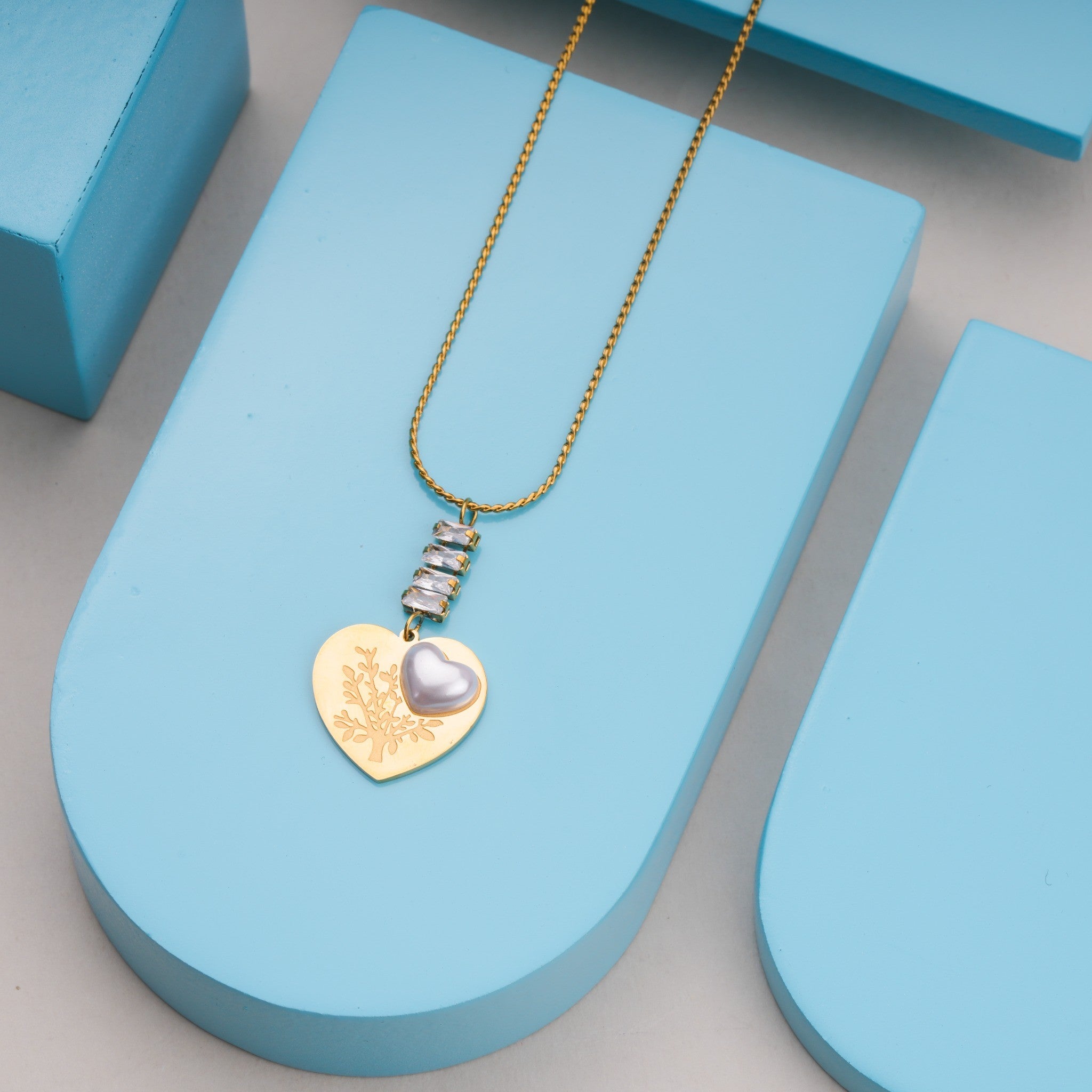 Gold chain necklace with heart-shaped pendant featuring floral engraving and silver heart accent on blue display