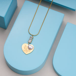 Gold chain necklace with heart-shaped pendant featuring floral engraving and silver heart accent on blue display