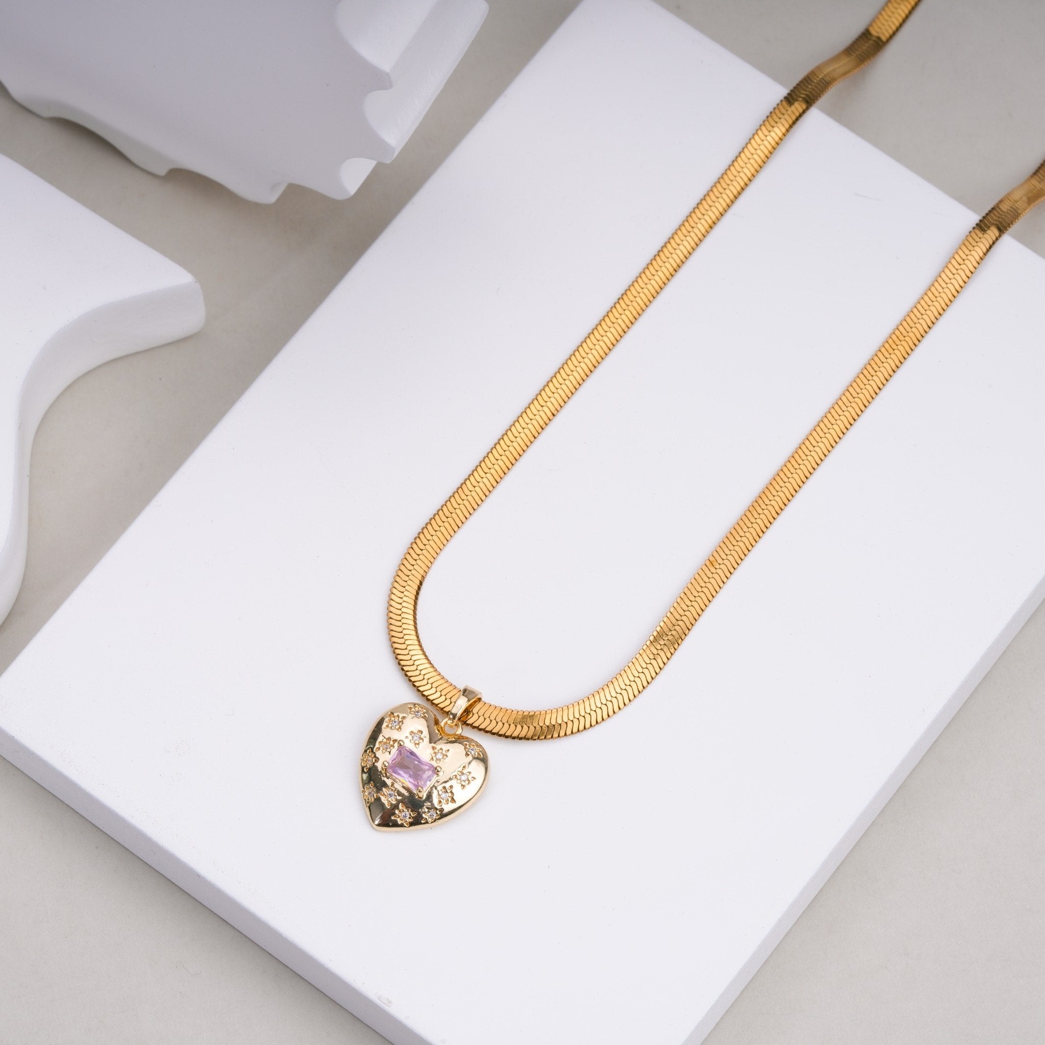 Gold chain necklace with heart-shaped pendant featuring a central purple gem and small floral patterns