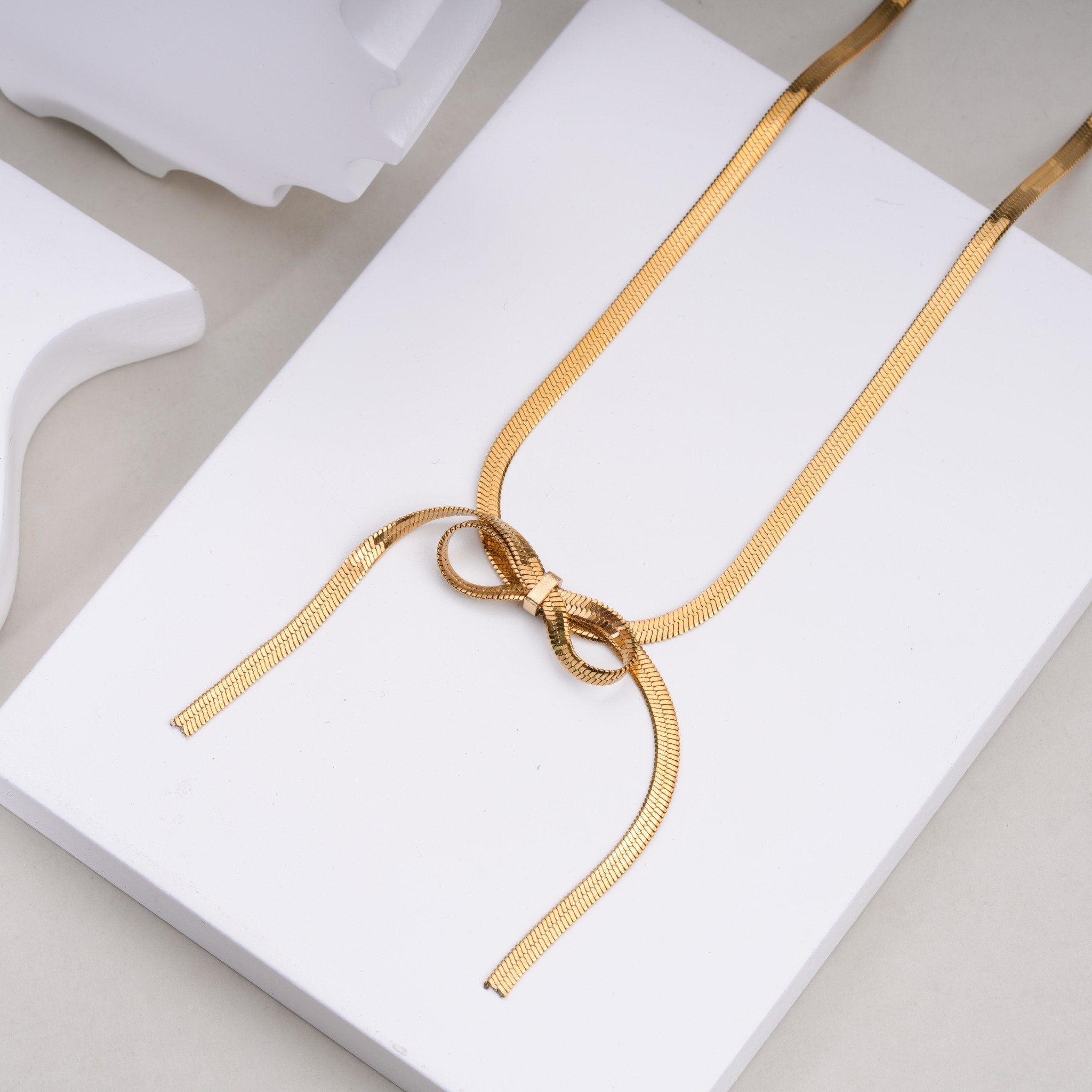 Gold bow-shaped fashion necklace on white display stand, elegant jewelry from Maniyar Bazaar