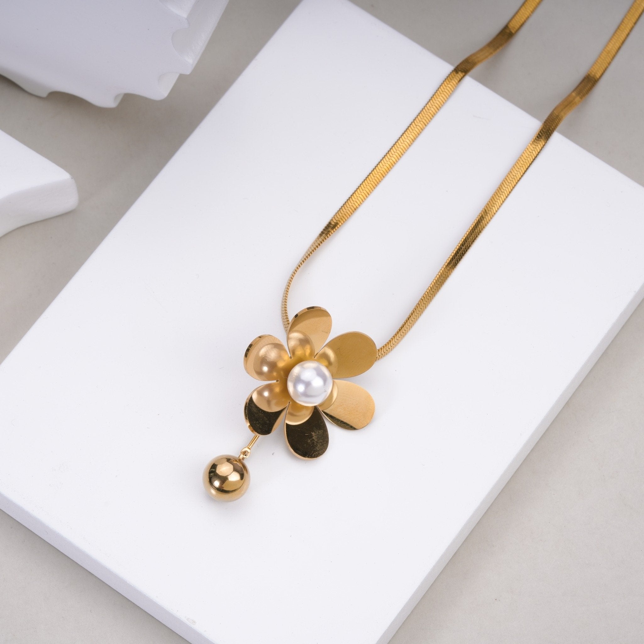 Gold flower pendant necklace with pearl center and dangling bead on white display