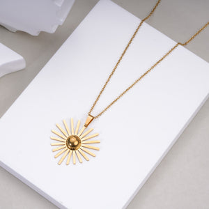 Gold sunburst pendant necklace on delicate chain displayed on white platform