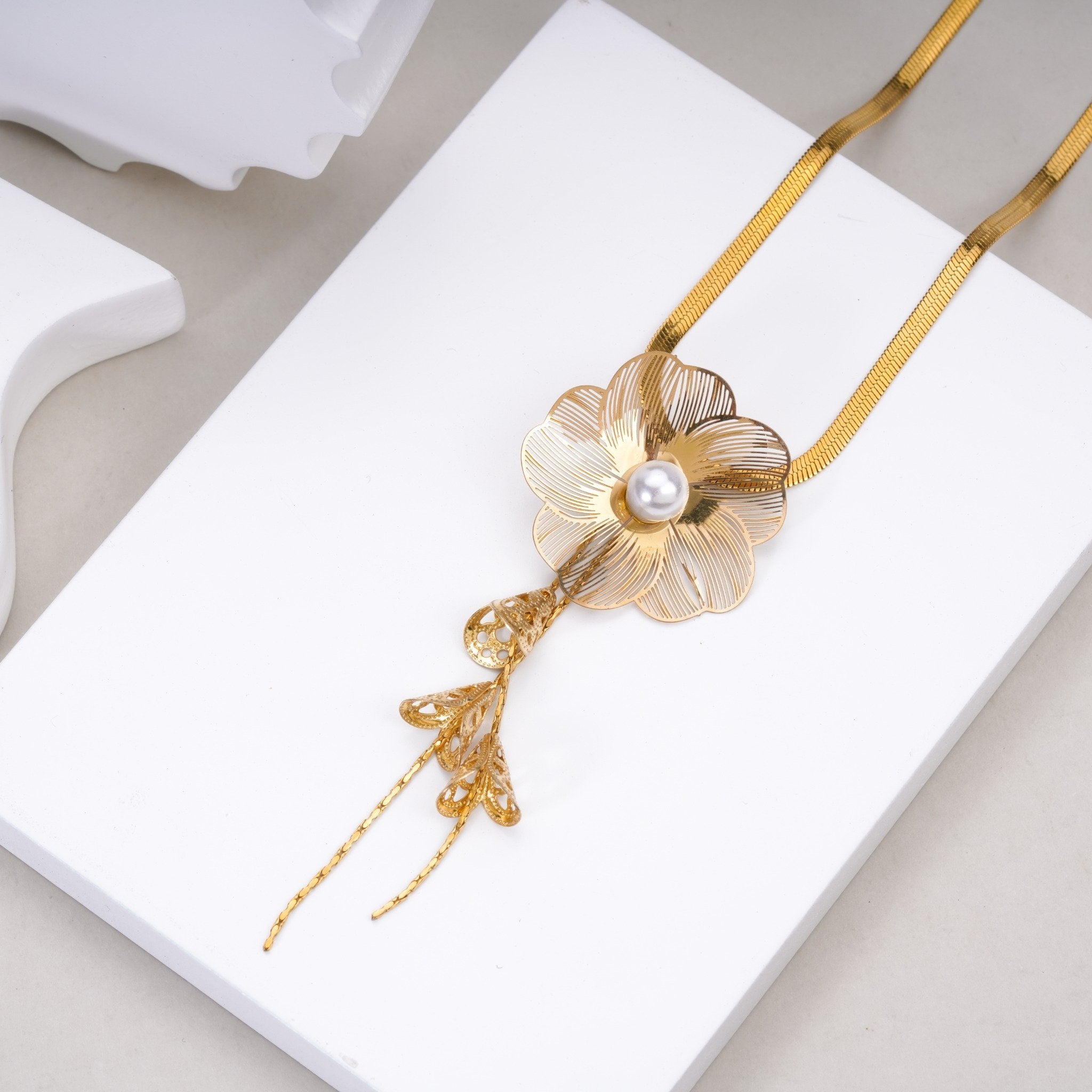 Gold floral pendant necklace with pearl center and intricate filigree design on white display