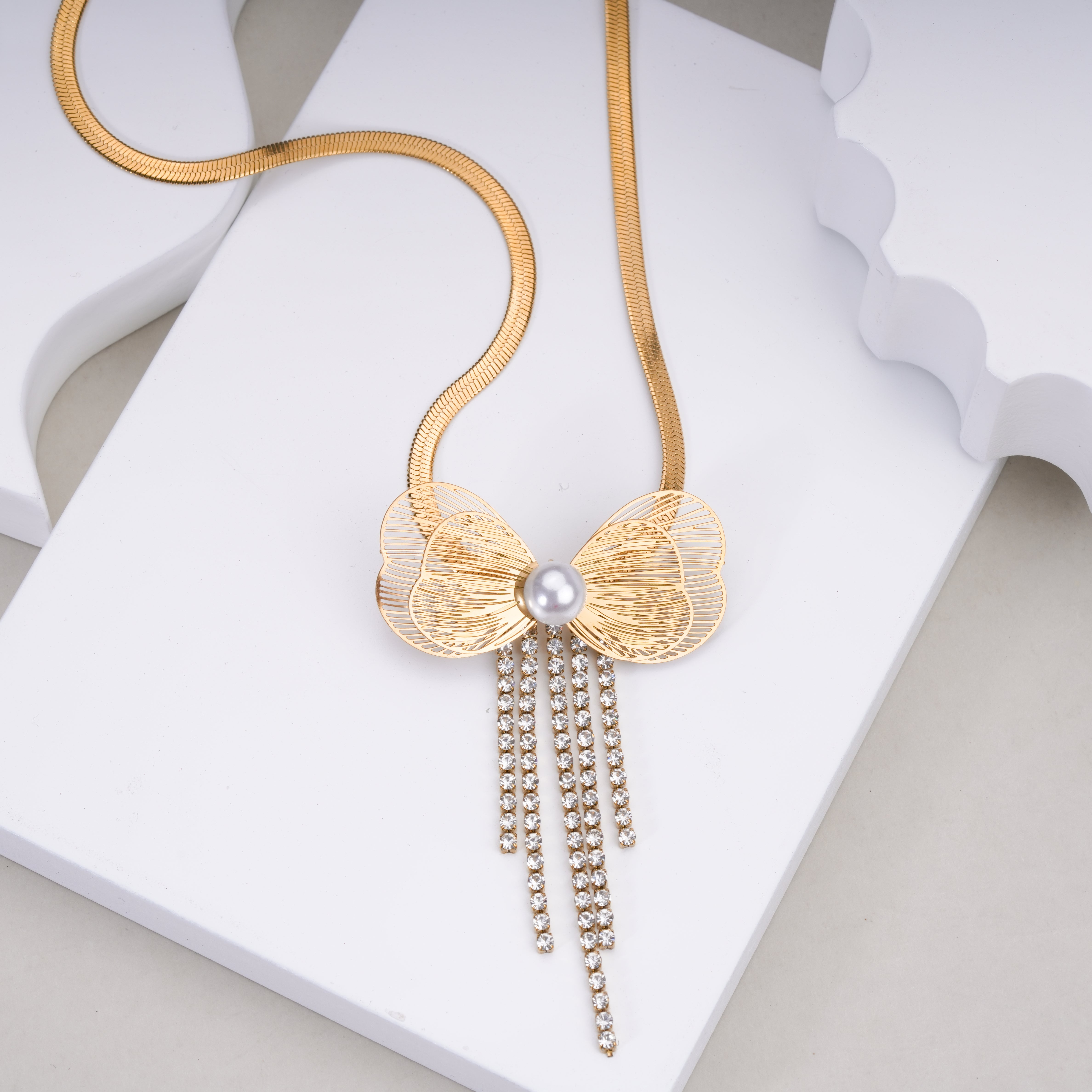 Gold butterfly pendant necklace with pearl center and dangling rhinestone chains on white background